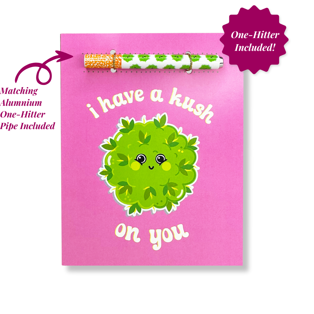 A cute and endearing greeting card with a soft pink background, adorned with a smiling cartoon cannabis bud and the pun 'I have a kush on you,'.